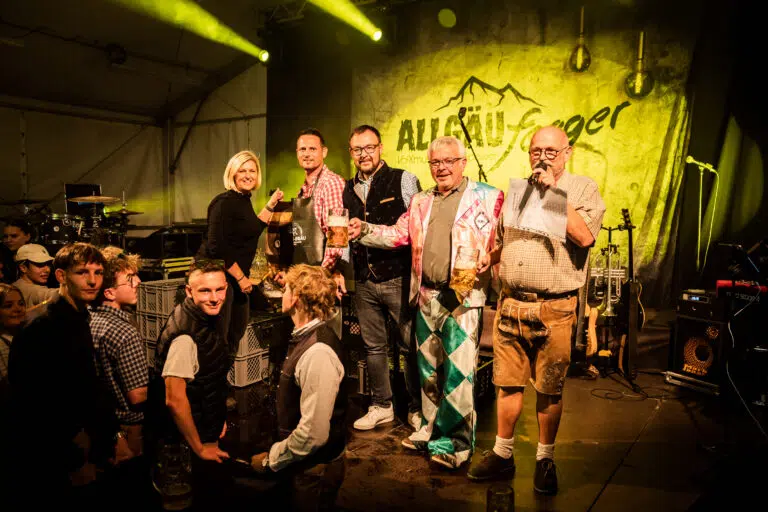 Festbesucher mit Bierkrügen und Tracht auf einer Bühne in Vorarlberg